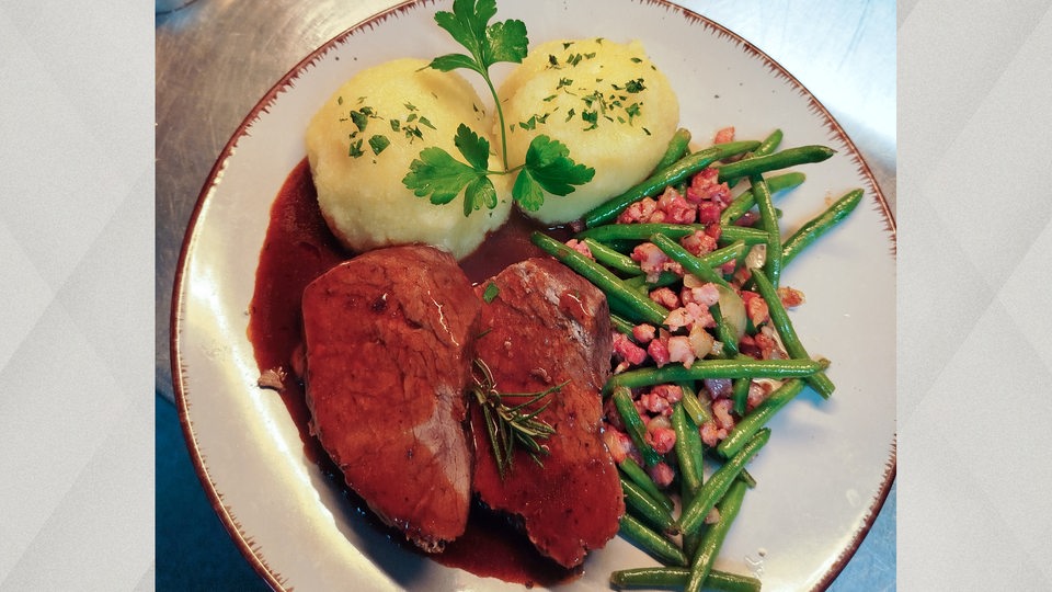 Ein Teller mit Braten und Soße, Speck und Bohnen und Klößen mit Petersilie