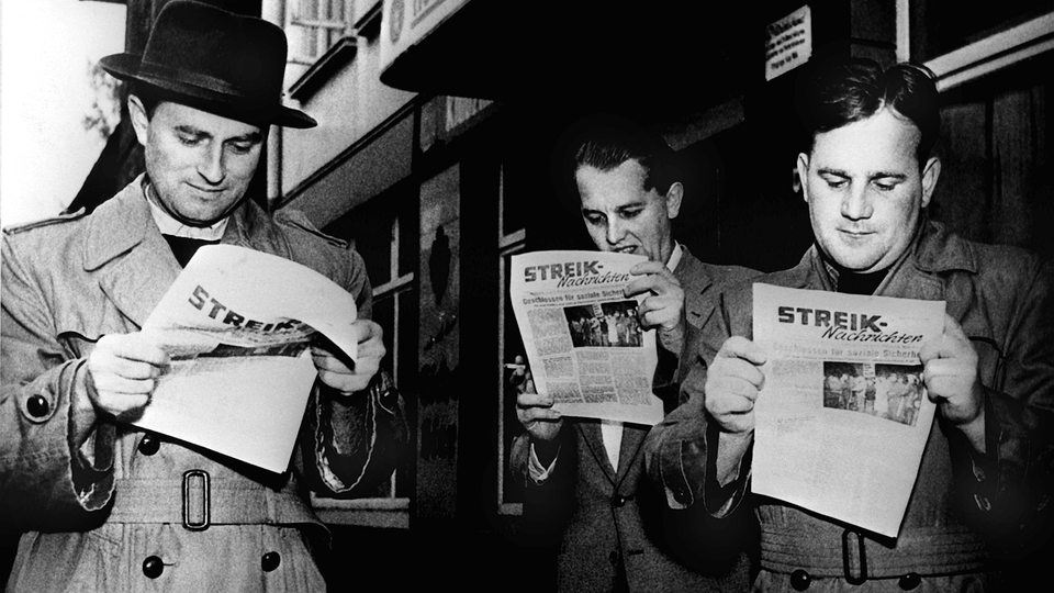 Streikende Arbeiter in Kiel lesen am 25.Oktober 1956, dem zweiten Streiktag, die neue vierseitige Streikzeitung der IG-Metall.